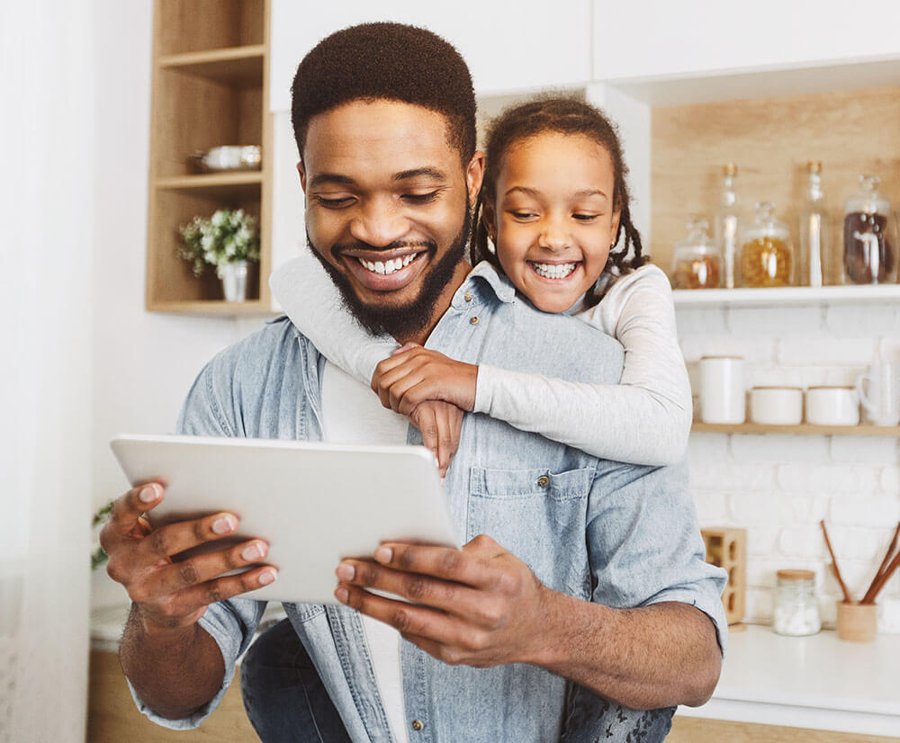 smiling father and young daughter looking at a tablet in their kitchen