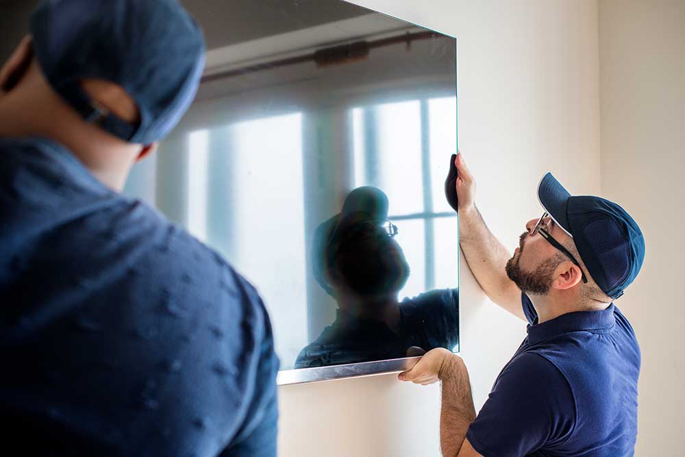 men in dark blue hats and shirts mounting a large flat display on a wall.